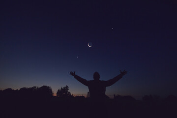 Wall Mural - silhouette of a man and countryside under the moon, stars and planets in blue hour time.