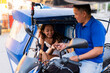 © Mdv Edwards - A cheerful Southeast Asian tricycle driver receives payment from a smiling young woman, sharing a friendly and positive street moment.