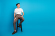 © deagreez - Young male sitting on stool in stylish casual attire against vibrant blue background
