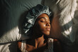 © Mariia Reimche - Young woman of African descent lying in bed with teal satin bonnet, peaceful expression and warm light, ideal for beauty, wellness, lifestyle content
