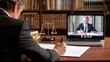 © intha - A lawyer in a study writes on documents while attending a virtual meeting with a client on a laptop.