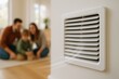 © michnik101 - Close-up of a wall air vent emitting air in a modern living room where a family sits together in the background.
