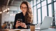 © Bog - The woman engaged with her smartphone in a modern workspace setting.