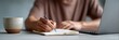 © olga_demina - Freelancer writing notes in notebook while working remotely on laptop with coffee mug nearby, enjoying work and travel lifestyle as digital nomad