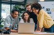 © Danny - Happy diverse creative team collaborating on project using laptop in modern office