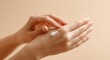 © Shelley - Close-up of a woman applying cream to her hand against a beige background, offering ample space for text or product details.