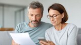 Couple sitting on sofa at home managing home finances, using smartphone and analyzing documents, calculating house expenses, planning mortgage or rent, making investment decision in real estate