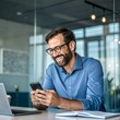 © Taposh - Smiling businessman using smartphone at his desk in modern office