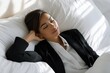 © Iryna - Young asian female relaxing in bed wearing business attire