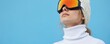 © Pete - Woman in ski goggles and white turtleneck looking up against blue background. She wears a knitted hat. Winter sport and fashion style, cold weather adventure and fun vacation.