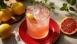 © Pete - Pink grapefruit cocktail with ice served on red plate, surrounded by lemons, plants. Juicy fruit beverage refreshing summer drink. Delicious citrus refreshment, cool tasty cocktail garnised with