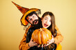 © Volodymyr - Woman witch with Pumpkin and man in witch hat. Halloween couple with pumpkin and Halloween makeup. Man and woman in witch hat celebrating Halloween.