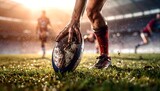 Close-up of a rugby player's hand placing a muddy rugby ball on the grass field during a match, with other players visible in the background.