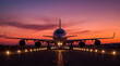 © DNA STUDIO - A commercial airplane is positioned on a runway its headlights and surrounding lights glowing The sky is painted with dramatic hues of orange pink and purple during sunset
