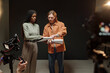 © TrueFrame Collective - Young Black woman and young Caucasian man rehearsing script together during acting audition, standing side by side in studio while film crew recording with professional cameras