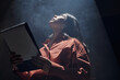 © TrueFrame Collective - Young adult Hispanic woman standing under spotlight holding script looking upward during acting audition, long dark hair visible, dramatic lighting emphasizing facial features