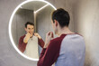 © StockMediaSeller - Young man flosses his teeth in front of a circular mirror, carefully maintaining oral hygiene as part of his daily dental care routine.