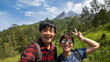 © Rizky - Happy Young asian couple wearing carrier mountain backpack is doing hiking activity together at Mount Merapi, Yogyakarta. Concept for outdoor activity and summer holiday hiking season.