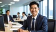 © saokaew - Professional businessman in a tailored suit sitting at a modern desk with a laptop and notepad in an office environment