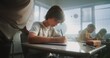 © Framestock - Elementary School Students Sitting and Writing Exam on Renewable Energy Resources in Modern Classroom. Female Teacher Walking Between Desks, Controlling Young Boys and Girls During School Test Process