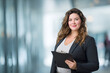 © Mariia Reimche - Confident plus-size businesswoman with clipboard in modern office, professional, approachable, soft corporate background, ideal for business, HR visuals. Cope space. managerwoman, leadership, smart