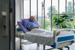 © BJ Day Stock - Asian woman cancer patient sitting alone on a hospital bed receiving saline and looking outside window in hospital ward with feeling of stress and lonely.