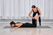 © TRAVELARIUM - In serene studio, female instructor aids adult woman in bow pose. Women, positioned on yoga mats, embody focus and precision, creating tranquil ambiance