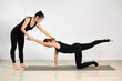 © TRAVELARIUM - Two young women in black outfits practice yoga on gray mat in bright studio. One assists other in achieving balanced pose, creating calm and focused atmosphere