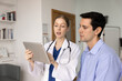 © fizkes - Serious young medical specialist woman explaining checkup report, diagnosis, test results on tablet, showing touchscreen to man in clinic doctor office, talking to patient after diagnosing examination