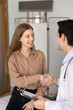 © fizkes - Cheerful young 20s female patient thanking physician for medical consultation, help, advice, shaking hands with practitioner, meeting with doctor after successful effective treatment. Vertical shot