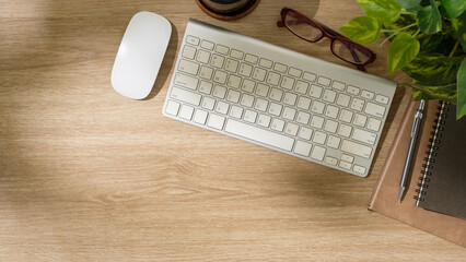 Wall Mural - Top view of modern workspace with wireless keyboard, mouse, notebook, pen, and plant on wooden desk.