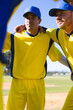 © Wavebreak Media - Two male baseball teammates standing in huddle at ballpark wearing yellow jerseys, blue caps