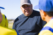 © Wavebreak Media - Male coach instructing players in yellow jerseys on grass field wearing baseball cap and navy shirt