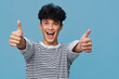 © SHOTPRIME STUDIO - smiling man in striped shirt showing double thumbs up with joyful expression on blue background, young adult, casual style, positive emotion, studio lighting
