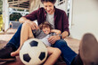 © Marko Geber - Portrait of a father and son sitting on a balcony and smiling while holding a soccer ball at home