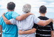 © luciano - Rear view of a family group of three multigenerational people, father, son and nephew together outdoors by the seaside feeling affection, care, freedom and vacation