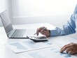© Zohara - A persons hands operate a calculator and pen over financial documents with a laptop in the background