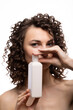 © Alina Zavhorodnii - Portrait of an attractive cheerful long-haired curly-haired girl holding a bottle of soap, shampoo, shower cream, on a white background Mockup