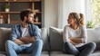 © Angelo - A young couple, a man and a woman, sitting on a sofa, looking upset during a disagreement.