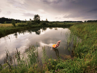 Wall Mural - a man is jumping into a pond wearing an orange swimsuit at dusk. the sky is cloudy and the water is 