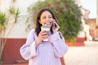 © luismolinero - Young woman at outdoors using mobile phone and holding a coffee with happy expression