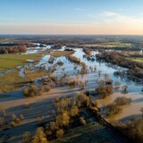 An expansive aerial perspective captures the flooding of a natural landscape, portraying the raw power of nature. The water inundates fields and trees.