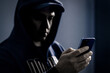 © terovesalainen - Phone and mobile hacker, thief and scammer. Protect digital data for scam, fraud or identity theft by cyber criminal. Crime with cellphone. Suspicious man in dark. Online romance fraudster.