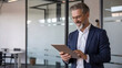 © Shamim - Confident senior businessman smiles while working on his tablet in a modern, bright office space, showcasing professional success and digital engagement.