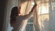 © ryker - Woman adjusts white linen curtains in softly lit room, allowing warm sunlight to filter through. serene atmosphere evokes sense of calm and tranquility