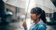 © Inkworksprint - A thoughtful young woman with a ponytail holds a transparent umbrella, looking sideways during a rainstorm.