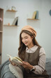 © WMSTUDIO - Young woman reading a book in cozy living room, wearing stylish outfit and fashionable beret, enjoying leisure time in modern interior space