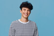 © SHOTPRIME STUDIO - smiling man wearing striped shirt stands against solid blue background, joyful expression with curly hair, casual style portrait of young adult male