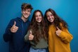 © Iftikhar alam - Teenage friends celebrating friendship with thumbs up in front of vibrant blue background during a casual gathering
