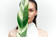 © VICHIZH - Young woman elegantly posing with a green leaf, showcasing natural beauty and simplicity in a minimalist setting.